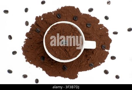 Kaffeepulver in weißer Tasse auf Hintergrund aus gemahlenem Kaffee, Ansicht von oben Stockfoto
