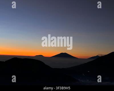 Friedliche Morgenlandschaft mit geschichteten Berg- und Vulkansilhouetten vor einem Himmel mit Farbverlauf von tiefblau zu orange. Stockfoto