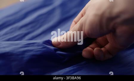 Männerhand prüft blauen Kunststofftaschenstoff Stockfoto