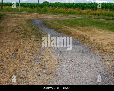 Kurviger Kiesweg, der sich durch trockenes Gras und grüne Felder in Coesfeld, Deutschland, schlängelt Stockfoto