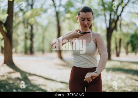 Fitnessfrau verwendet Smartphone und Smartwatch während eines Outdoor-Fitness-Workouts im Park Stockfoto