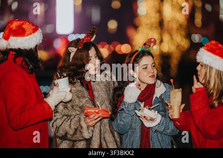 Vier Freunde feiern Weihnachten im Freien bei Nacht mit Weihnachtsmannmützen und festlichen Accessoires Stockfoto