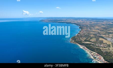 Luftbild der Kassandra-Küste in Griechenland mit klarem blauem Meer, Küstenlinie, landwirtschaftlichen Feldern und verstreuten Gebäuden unter einer teilweise bewölkten Stockfoto