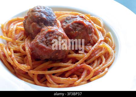 Nahaufnahme von vorne auf Spaghetti mit Tomatensoße und drei Fleischbällchen in einer weißen Pastaschüssel bei hellem natürlichem Licht Stockfoto