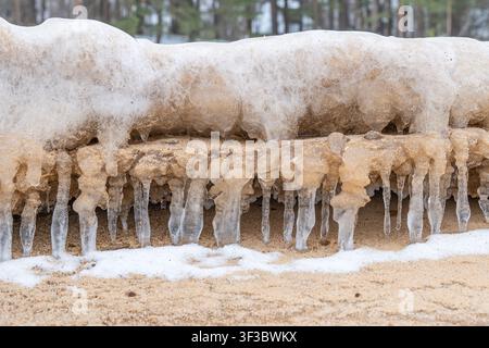 Gefrorener Sand und Eisscholle mit hängenden Eiszapfen am winterlichen Ostseustrand, Nahaufnahme der natürlichen Küstenabrasion, die eine rohe Textur erzeugt, kalte Stille und Quie Stockfoto