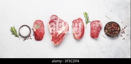 Auswahl an frischen rohen Rindersteaks mit Gewürzen auf Steintisch. Flache Lage von oben Stockfoto