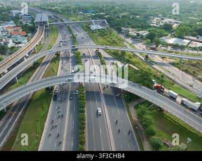 Luftaufnahme eines belebten mehrstufigen Autobahnkreuzes, einer erhöhten Eisenbahnstrecke und eines städtischen Verkehrsnetzes, umgeben von Grünflächen in Ho-Chi-Minh-Stadt, V Stockfoto