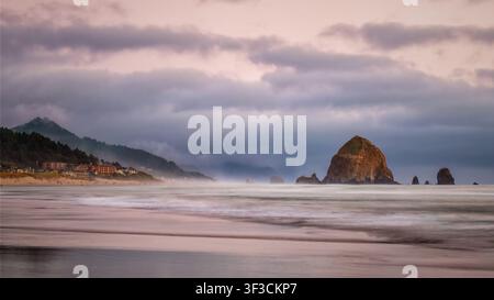 Haystack Rock in Cannon Beach, Oregon, USA mit Wellen und Wolken im Abendlicht Stockfoto