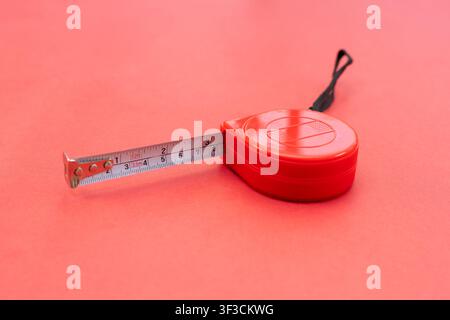 Rotes einziehbares Taschenmaßband mit Gurt auf rotem Hintergrund Stockfoto