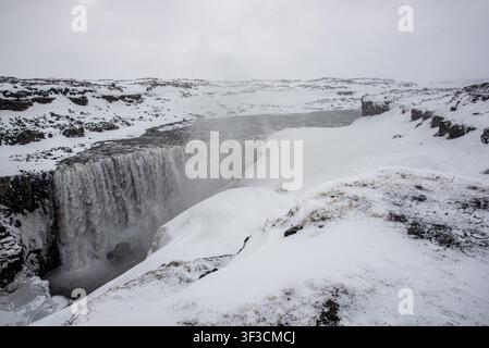 Der mächtige isländische Dettifoss-Wasserfall fließt kraftvoll zwischen felsigen Schluchten und völlig schneebedeckten Klippen. Ein dichter Wasserdunst steigt auf von Stockfoto