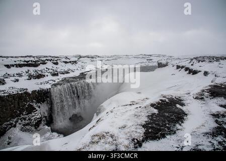 Der mächtige isländische Dettifoss-Wasserfall fließt kraftvoll zwischen felsigen Schluchten und völlig schneebedeckten Klippen. Ein dichter Wasserdunst steigt auf von Stockfoto