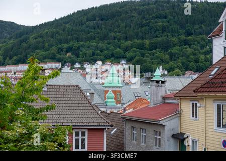 Bezaubernde Dächer von Bergen mit kunstvollen grünen Kupfertürmen, farbenfrohe Häuser, die den Hügel hinaufklettern, bedecktes nordisches Licht, ideal für Reiseeditorial. Stockfoto