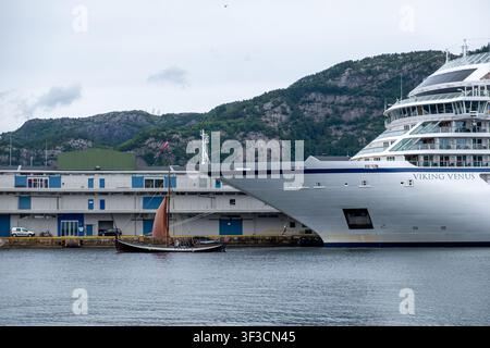 Auffälliger Größenkontrast zwischen einem modernen Kreuzfahrtschiff und einem historischen Holzsegelboot im Hafen von Bergen, Norwegen. Stockfoto