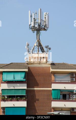 Viladecans, Spanien – 23. Juli 2026: Niedrigwinkelaufnahme von Mobilfunknetzsendern und Mikrowellenschüsseln, die auf dem Dach eines städtischen Wohngebäudes installiert sind Stockfoto
