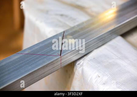 Ein Stahlvierkantrohr, das mit roten Bleistiftlinien für das Schneiden und Schweißen auf dem Werkstatttisch markiert ist, Nahaufnahme zeigt Metalltextur und Messanleitungen Stockfoto