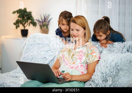 Mutter arbeitet von zu Hause aus am Laptop mit Kindern, die zuschauen Stockfoto