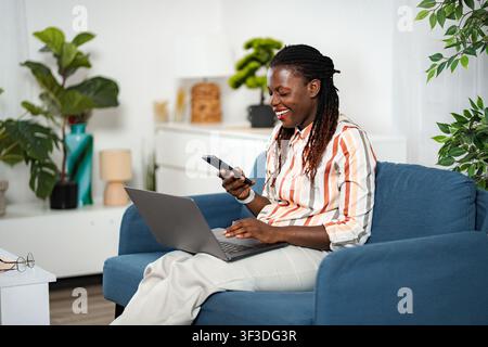Afroamerikanische Frau arbeitet von zu Hause aus mit Laptop und Telefon Stockfoto