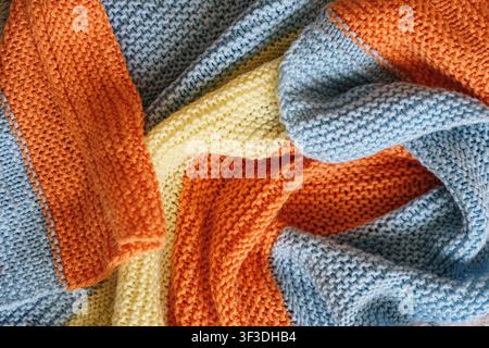 Weiche Strickdecke in Pastellblau, Creme und Orange. Gemütlicher strukturierter Stoffhintergrund mit warmer Wohnatmosphäre. Stockfoto