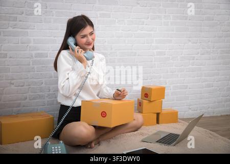 Frau erhält Anweisungen über ein Retro-Telefon. Erfolgreiche Unternehmerin mit Online-Verkäufen und Paketversand in ihrem Homeoffice. Stockfoto