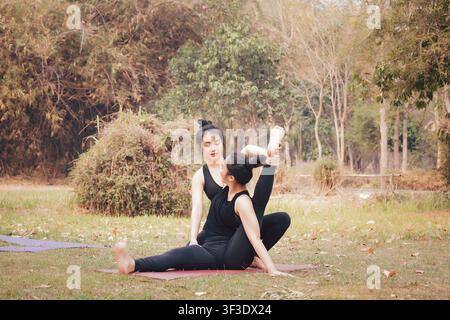 Yoga-Lehrer hilft, die Haltung eines Schülers in einem Outdoor-Kurs anzupassen. Konzept für Yoga-Übungsunterricht. Stockfoto