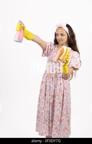 Lächelnde junge weibliche Haushälterin hält Sprühflasche und gelben Schwamm Stockfoto