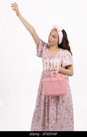 Glückliche junge Frau hebt die Hand und hält eine rosa Handtasche in gehobener Stimmung Stockfoto