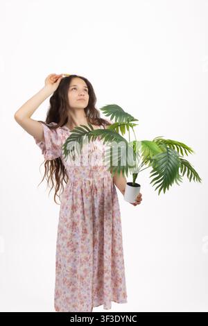 Junge lächelnde Frau hält ein großes grünes Monstera-Blatt nahe ihrem Gesicht Stockfoto
