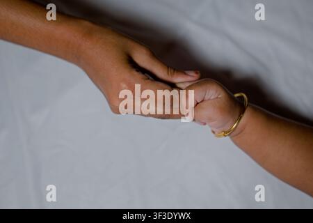 Zarte Nahaufnahme einer winzigen Hand eines Säuglings, die den Daumen eines Elternteils hält, symbolisiert elterliche Liebe, Sicherheit, Fürsorge und familiäre Bindung auf einem weichen Weiß Stockfoto
