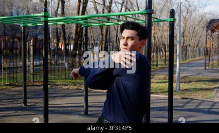 Athletische junge Frau streckt ihre Arme in der Nähe von Outdoor-Workout-Geräten Stockfoto