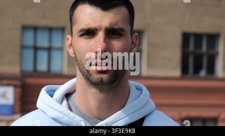 Porträt eines jungen selbstbewussten bärtigen Mannes in lässiger Kleidung mit Stadtbild-Hintergrund. Nahaufnahme eines gutaussehenden Kerls, der in die Stadt steht Stockfoto