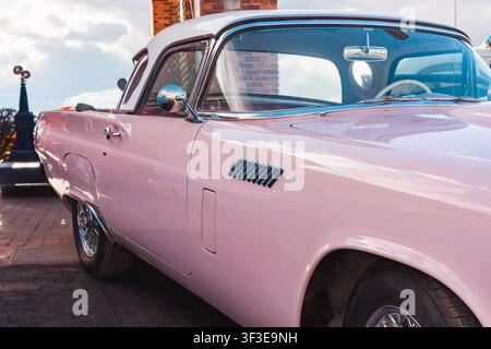 Vintage-rosa Ford Thunderbird der 1950er Jahre mit glänzenden Chromrädern und charakteristischen Seitenlüftungen, der das ikonische amerikanische Retro-Autodesign präsentiert Stockfoto