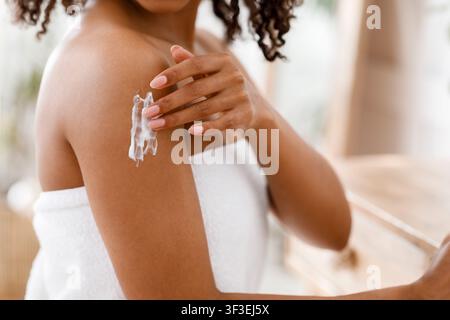 Schwarze Frau Anwendung feuchtigkeitsspendende Körperlotion auf die Haut nach der Dusche Stockfoto