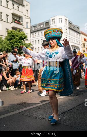 Berlin, Deutschland - 24. Mai 2026. Eine ecuadorianische Frau tanzt in einem bestickten türkisfarbenen Kleid und einem aufwendigen traditionellen Kopfschmuck während des Karnevals der Stockfoto