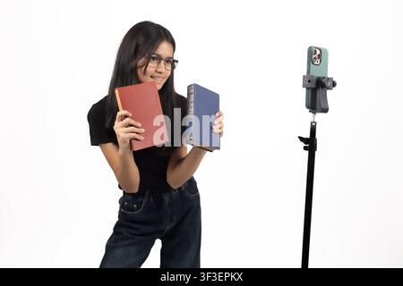 Weibliche Streamerin hält Bücher, während sie einen Podcast am Mikrofon aufnimmt Stockfoto