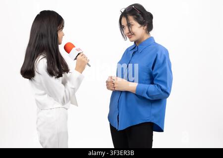 Frau Reporterin interviewt eine andere Frau mit Mikrofon im Innenraum Stockfoto