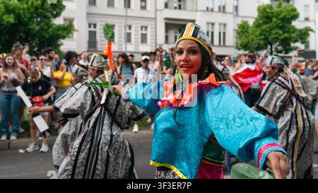 Berlin, Deutschland – 24. Mai 2026. Eine lächelnde Frau in einem lebhaften türkisfarbenen Kostüm führt Darsteller in geometrisch gemusterten Outfits während des Karnevals an Stockfoto