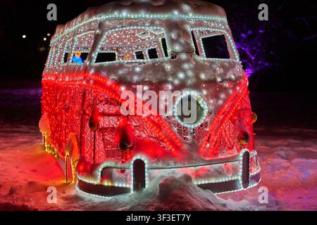 Eine beleuchtete Eisskulptur eines klassischen Volkswagen Type 2 Wohnmobils (VW Bus), bedeckt mit Schnee und verziert mit lebhaften roten und weißen LED-Lichtern. Stockfoto