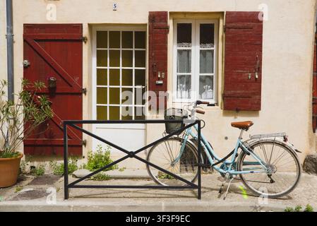 Ein grünes Fahrrad, das an einem traditionellen Wohnhaus mit lebhaften roten Holzläden in Arles, Frankreich, geparkt ist. Stockfoto