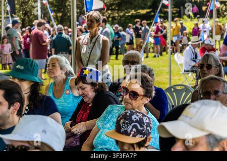 Besucher sitzen unter einem Festzelt bei den ‚Acadian Days‘ im Grand-Pré-Nationaldenkmal in Grand Pré, Nova Scotia, Kanada; mehrere tragen die Akadier-Flagge oder tragen Mützen in ihren Farben Blau, Weiß und Rot mit einem goldenen Stern Stockfoto