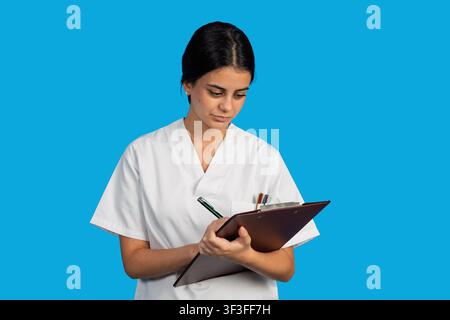 Gesundheitsfachkraft, die Patientenakten verwaltet, stehend vor einem blauen Hintergrund Stockfoto