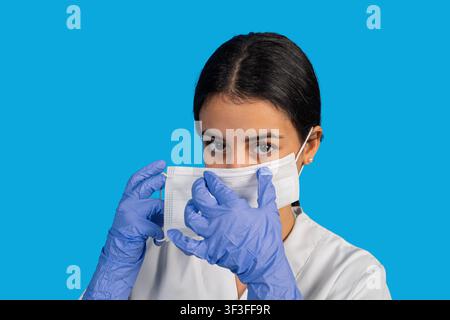 Junge Ärztin oder Krankenschwester trägt OP-Handschuhe und passt eine Schutzgesichtsmaske an Stockfoto