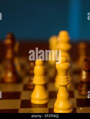 Nahaufnahme einer weißen Dame und eines Bauern vor verschwommenen schwarzen Figuren auf einem Schachbrett, ein konzeptioneller Kampf, bei dem Weiß Gutes symbolisiert und Schwarz Stockfoto