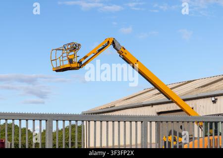 Gelber Scherenkran-Auffahrwagen über einer Industrieeinheit gegen blauen Himmel erhoben Stockfoto