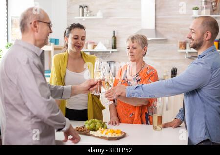 Erweiterte Familie stößt mit Weingläsern an während eines Küchenmittags, feiert gemeinsam rund um Essen, Konversation und multigenerationelles Familienleben, wobei Essen, Konversation und Familienbindung sichtbar sind. Stockfoto