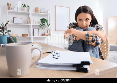 Junge Frau, die Stress und Angst verspürt, während sie von zu Hause aus arbeitet, sich an ihrem Schreibtisch überfordert und isoliert fühlt Stockfoto