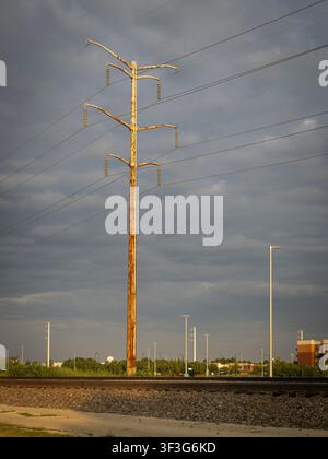 Ein hoher, verwitterter Holzstrommast steht neben Eisenbahngleisen unter einem dramatischen bewölkten Himmel in der Dämmerung Stockfoto