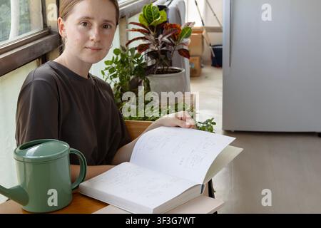 Junge Frau liest ein leeres Hardcover-Buch zu Hause mit einem grünen Gießkanne Stockfoto