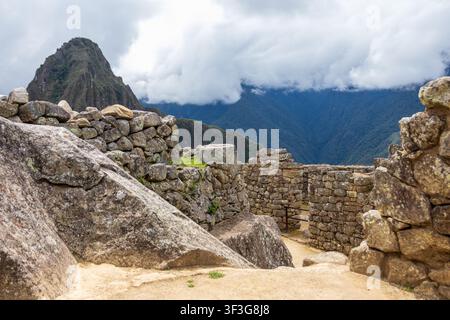 Blick auf die antiken Steinruinen von Machu Picchu mit dem hoch aufragenden Berg Huayna Picchu im Hintergrund unter einem bewölkten Himmel in Cusco, Cusco, Peru. Stockfoto