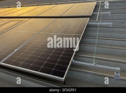 Nahaufnahme von photovoltaischen Solarpanelen, die auf einem Metalldach einer Industrieanlage installiert sind, mit Montageschienen und Erdungsbauteilen für erneuerbare Energien Stockfoto