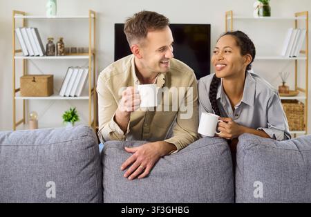Lächelnd genießt Kaffee zu Hause, entspannt auf dem Sofa und unterhält sich gemeinsam Stockfoto